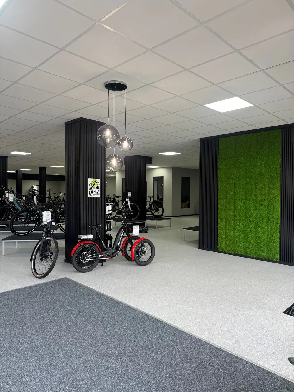 Ein heller Fahrradladen mit schwarzen Säulen, Leuchten, Mooswand und roten E-Bikes