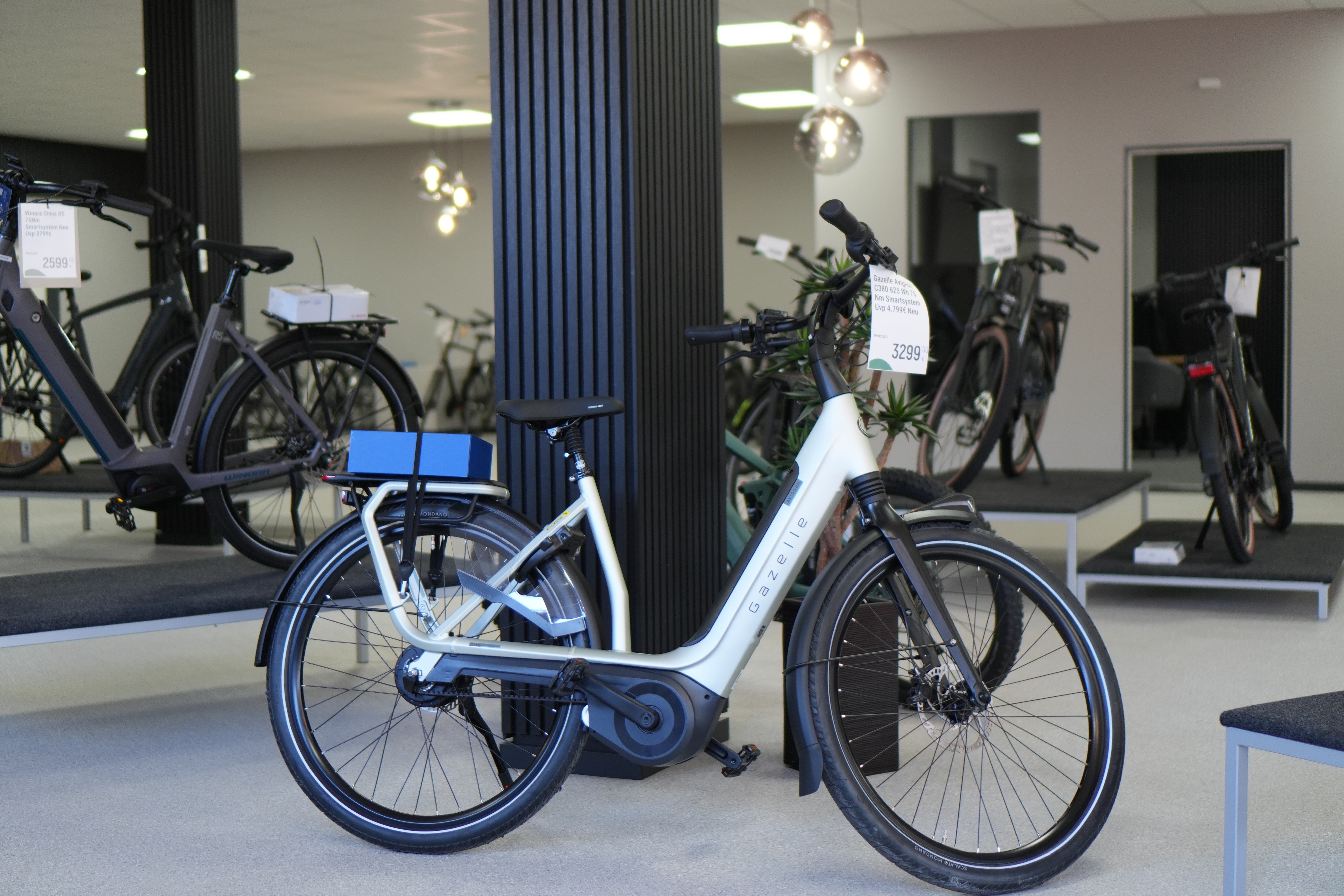 Ein hellblaues Elektrofahrrad steht in einem hellen Ausstellungsraum mit weiteren Rädern